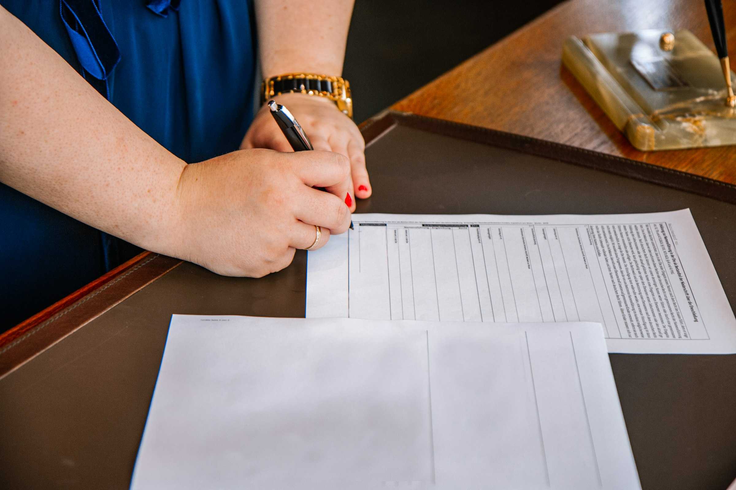 A hand signing a form at an office desk